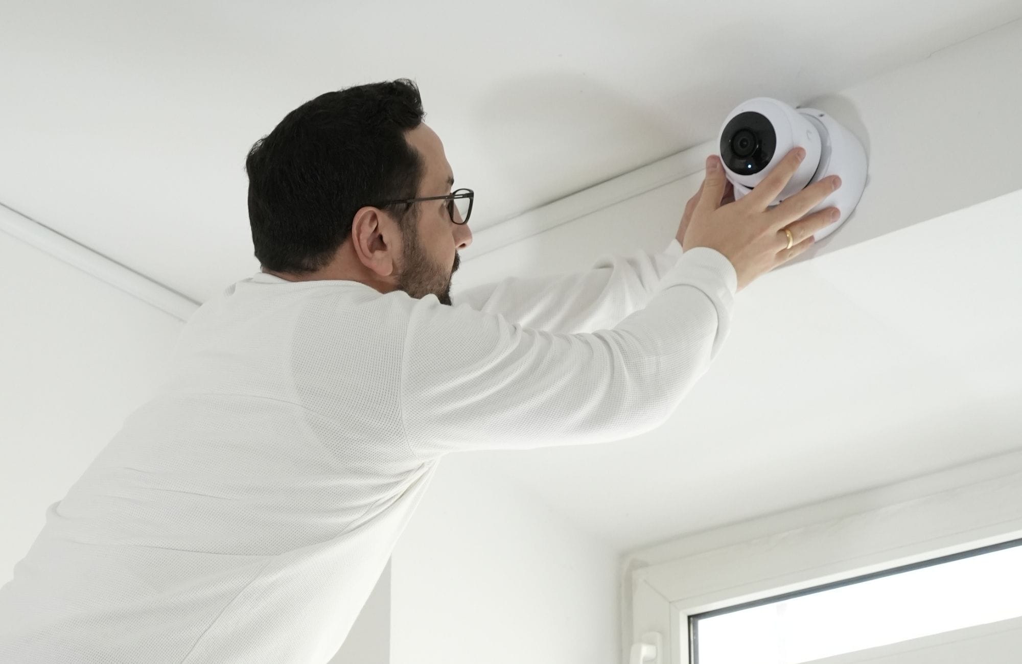 Kyrillos Poutakidis bringt mit beiden Händen eine moderne, weiße Kuppel-Überwachungskamera an einer Decke an. Das Foto veranschaulicht den professionellen Smart-Office-Service von syskypo für den Schutz Ihrer Geschäftsräume durch intelligente Objektsicherheit und zukunftssichere IT-Betreuung.