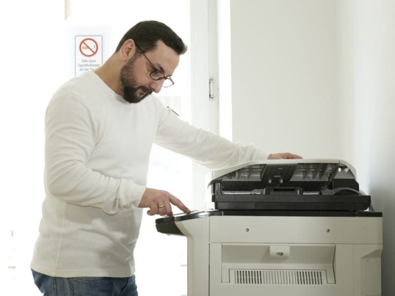Der IT-Dienstleister Kyrillos Poutakidis bedient konzentriert das Tastenfeld eines großen, modernen Multifunktionsdruckers im Büro. Die Szene zeigt den verlässlichen Support und die hardwareübergreifende IT-Betreuung von syskypo für reibungslose und störungsfreie Abläufe bei Ihren geschäftlichen Dokumenten.