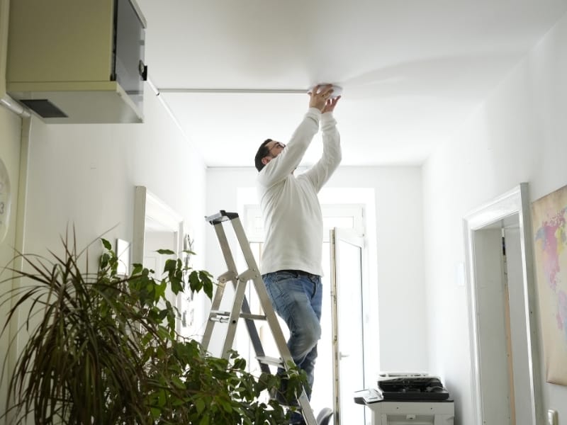 IT-Experte Kyrillos Poutakidis steht auf einer Leiter in einem hellen Hausflur und montiert einen runden, weißen UniFi WLAN-Access-Point an der Decke. Das Foto dokumentiert den fachgerechten Vor-Ort-Service von syskypo für die Installation stabiler und optimal abgestimmter Netzwerke im Betrieb.