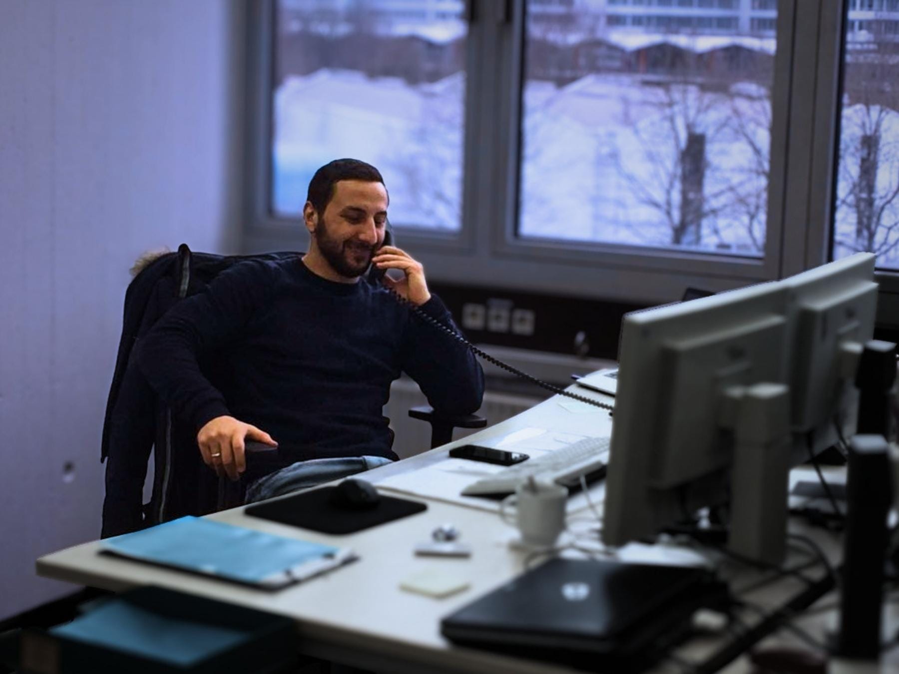 Kyrillos Poutakidis, Gründer von syskypo, sitzt lächelnd an seinem Büro-Schreibtisch mit Computermonitoren und führt ein persönliches Telefongespräch über verlässliche IT-Betreuung und IT-Dienstleistungen.