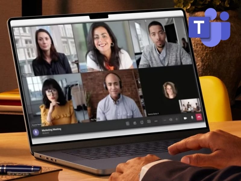 Ein geöffneter Laptop auf einem Holztisch zeigt eine aktive Microsoft Teams Videokonferenz mit fünf Teilnehmenden in einer Kachelansicht. Oben rechts ist das violette Microsoft Teams-Logo zu sehen, während eine Hand auf der Tastatur liegt. Dieses Bild symbolisiert die ortsunabhängige und nahtlose Zusammenarbeit im Team, die von Kyrillos Poutakidis über syskypo durch strukturierte IT-Dienstleistungen und moderne IT-Betreuung in der Cloud eingerichtet wird.